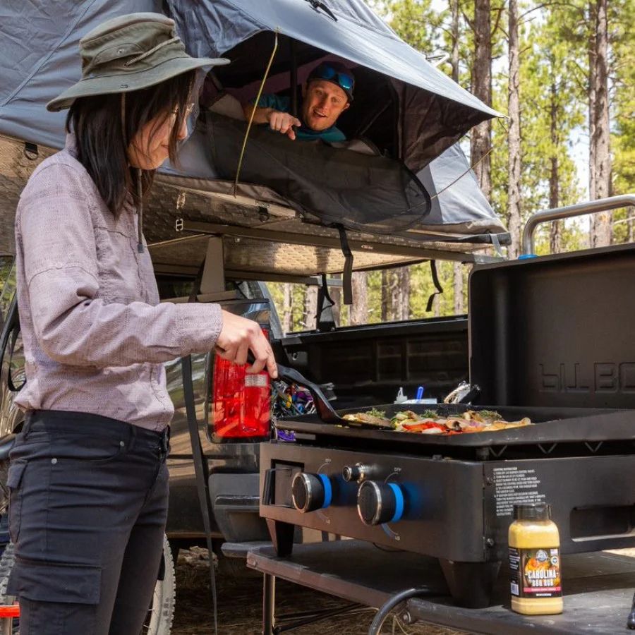 Woman cooking outdoors with food on the Pit Boss 2-Burner Griddle while camping