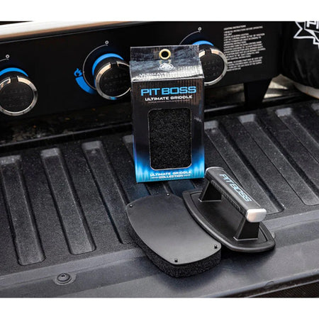 A Pit Boss Ultimate Griddle Scrub Brush with a black replacement pad attached, resting on a griddle.