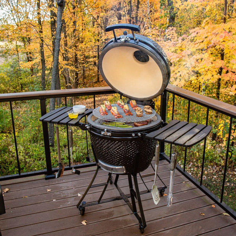Louisiana Grills 24" Ceramic Kamado Charcoal Grill with open lid, grilling lobster tails, mushrooms, and asparagus on the stainless steel grates.