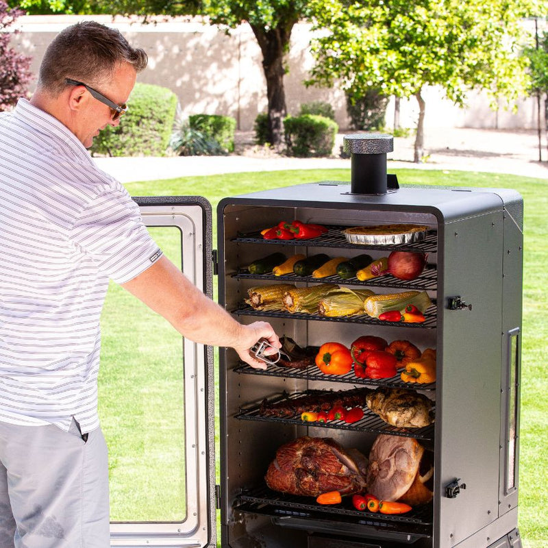 Man using the Louisiana Grills 7-Series Wood Pellet Vertical Smoker outdoors, adjusting the racks while smoking meats and vegetables, highlighting its spacious cooking area and even heat distribution.