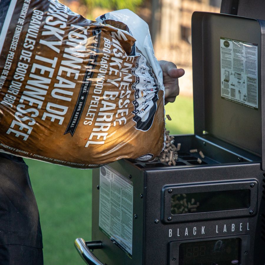 Pouring Tennessee Whiskey Barrel hardwood pellets into the Louisiana Grills 800 Black Label hopper for premium wood-fired cooking.