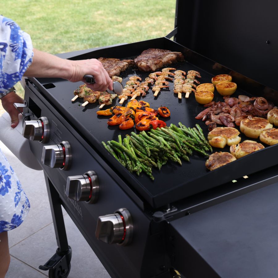 A close-up view of the Louisiana Grills Founders Series 4-Burner Gas Griddle cooking a variety of food, including grilled vegetables, shrimp skewers, and steak.