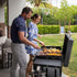 A couple enjoying outdoor grilling on the Louisiana Grills Founders Series 4-Burner Gas Griddle, cooking breakfast and meats on a backyard patio.