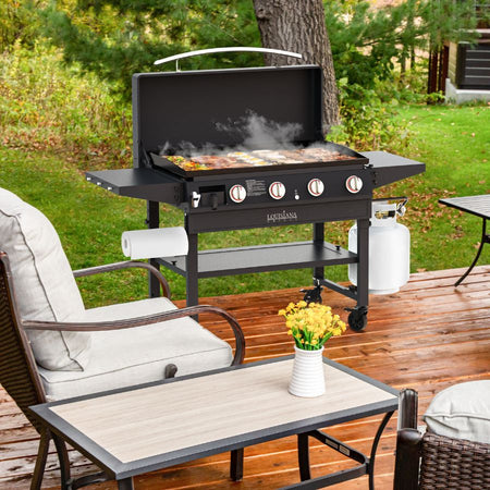 The Louisiana Grills Founders Series 4-Burner Gas Griddle set up on a wooden deck, steaming with food, surrounded by patio furniture and a natural outdoor setting.