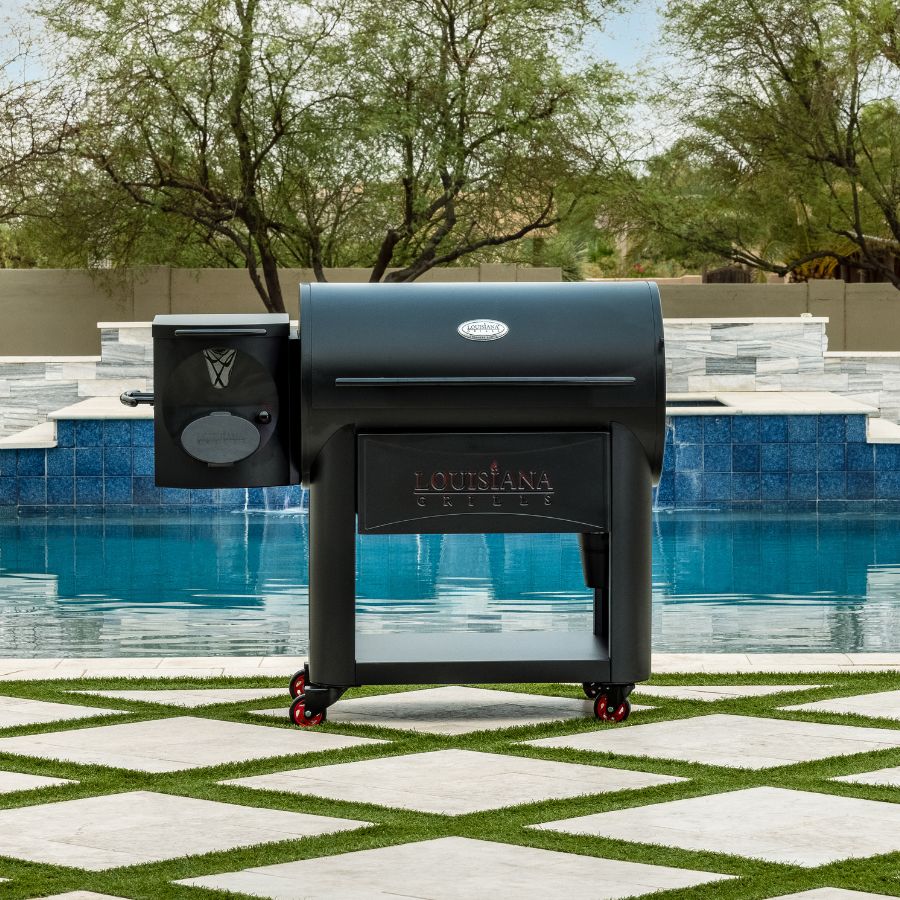 Louisiana Grills Founders Series Premier 1200 Pellet Grill placed outdoors by a luxurious swimming pool, showcasing its sleek black design and durable build.