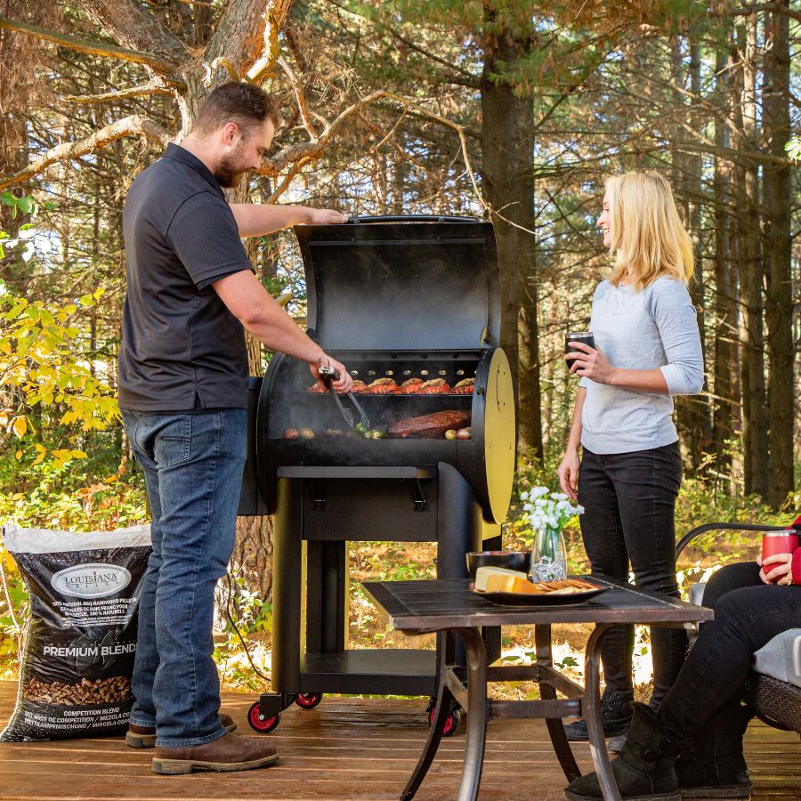 A couple grilling on the Louisiana Grills Founders Series Premier 800 Pellet Grill outdoors, enjoying a backyard barbecue experience.