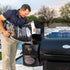 Man pouring premium wood pellets into the hopper of the Louisiana Grills Founders Series Premier 1200 Pellet Grill, demonstrating the easy fuel-loading process.