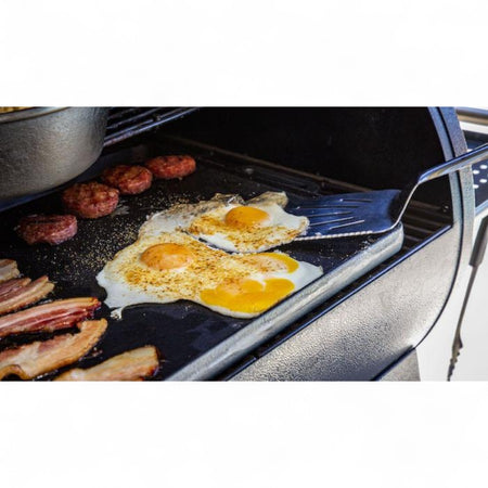 A close-up of bacon and fried eggs cooking on the Pit Boss 14" x 28" Cast Iron Griddle