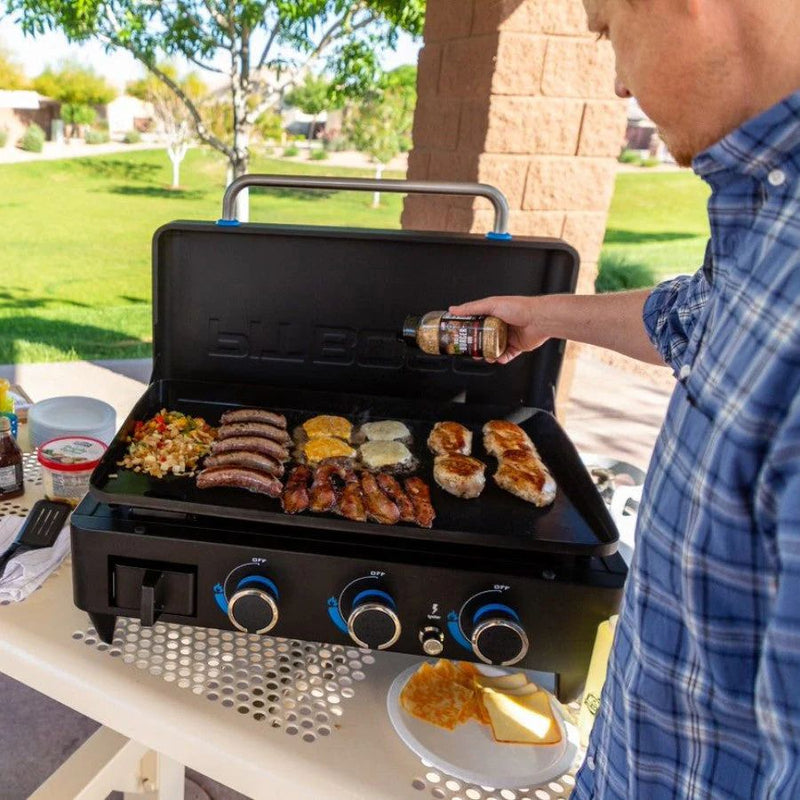 Man seasoning food on the Pit Boss 3-Burner Ultimate Griddle while grilling outdoors