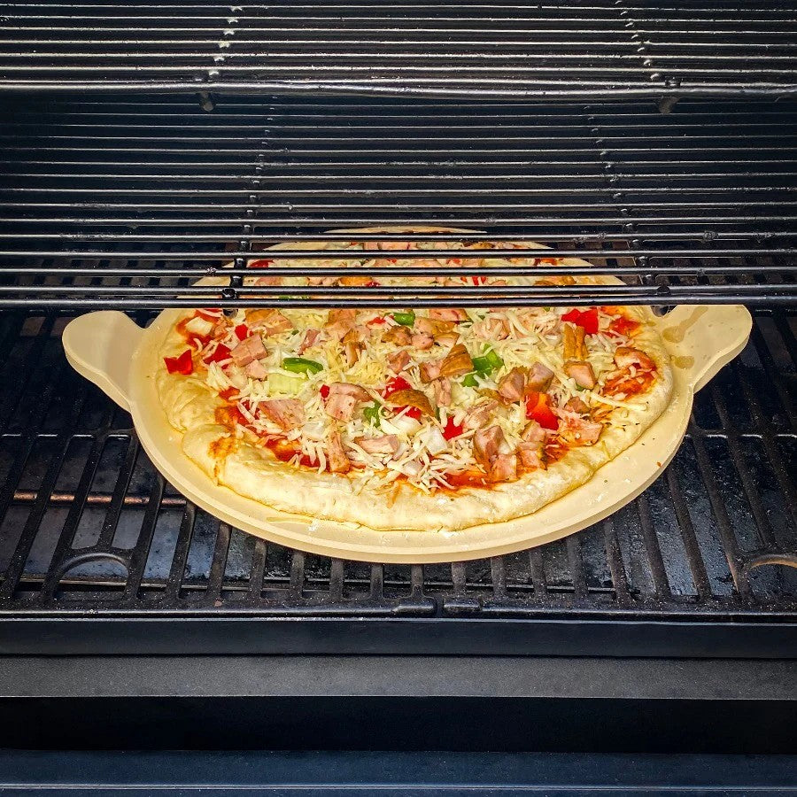 A Pit Boss 15-inch ceramic pizza stone with a golden-crusted pizza inside a grill