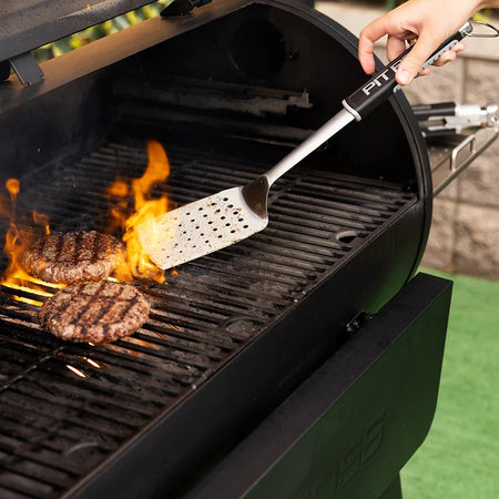 A person using the Pit Boss BBQ spatula to flip burgers on a grill with flames