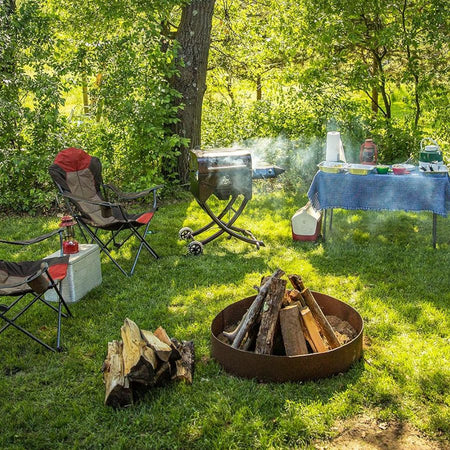 Pit Boss Mahogany 260 Portable Wood Pellet Grill in a campsite setting with camp chairs and fire pit
