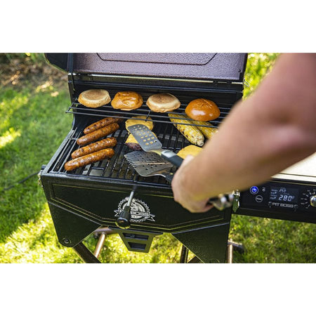 Person grilling sausages, buns, and corn on a portable grill outdoors.