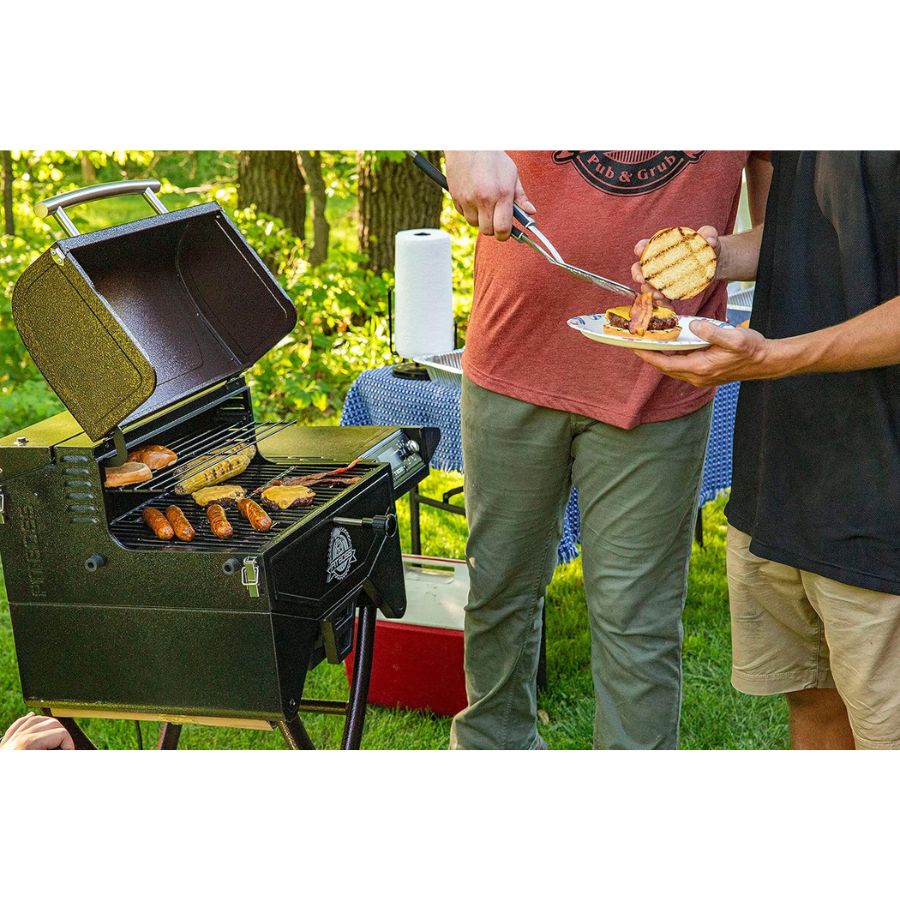 Two people grilling outdoors with a portable barbecue in a park setting.