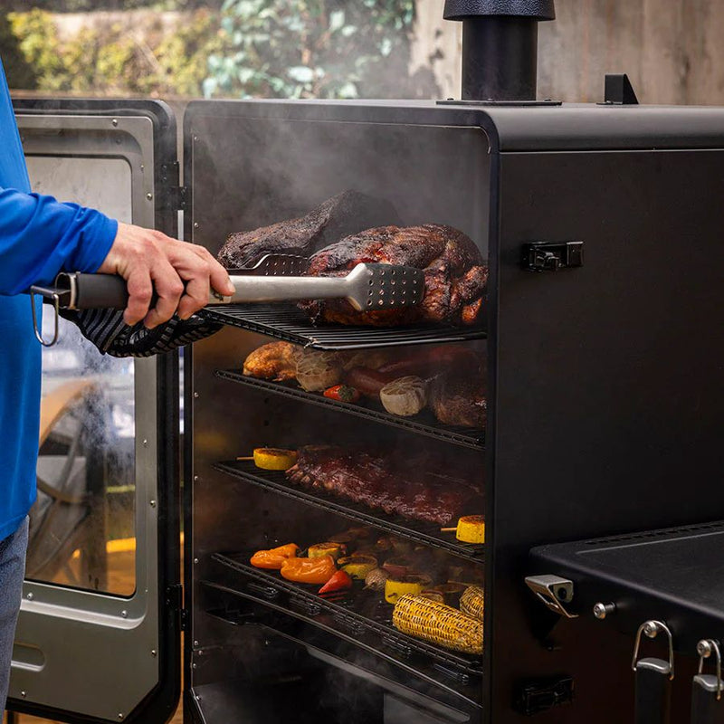 Person using tongs to adjust large cuts of smoked meat on the grill racks of the Pit Boss Navigator 6 Series.
