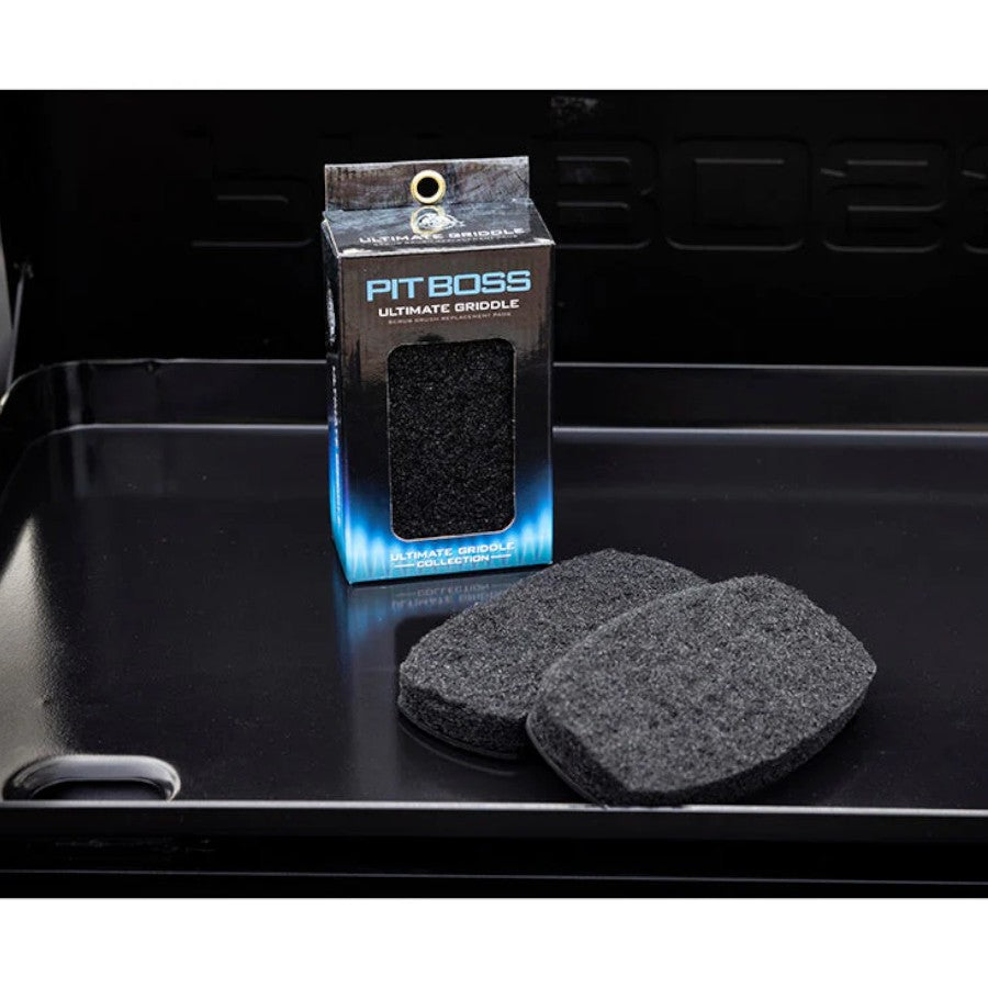 Packaging for Pit Boss Ultimate Griddle Scrub Brush Replacement Pads, with two pads outside the box, on a griddle surface.