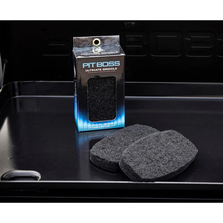 Packaging for Pit Boss Ultimate Griddle Scrub Brush Replacement Pads, with two pads outside the box, on a griddle surface.